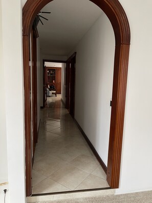Un couloir orné d’une arche en bois, qui mène à une pièce dont le sol est recouvert de carreaux et qui contient une chaise.