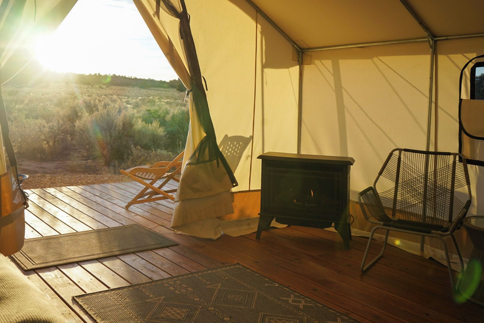 A tent with a wooden deck, a black stove, and two chairs.