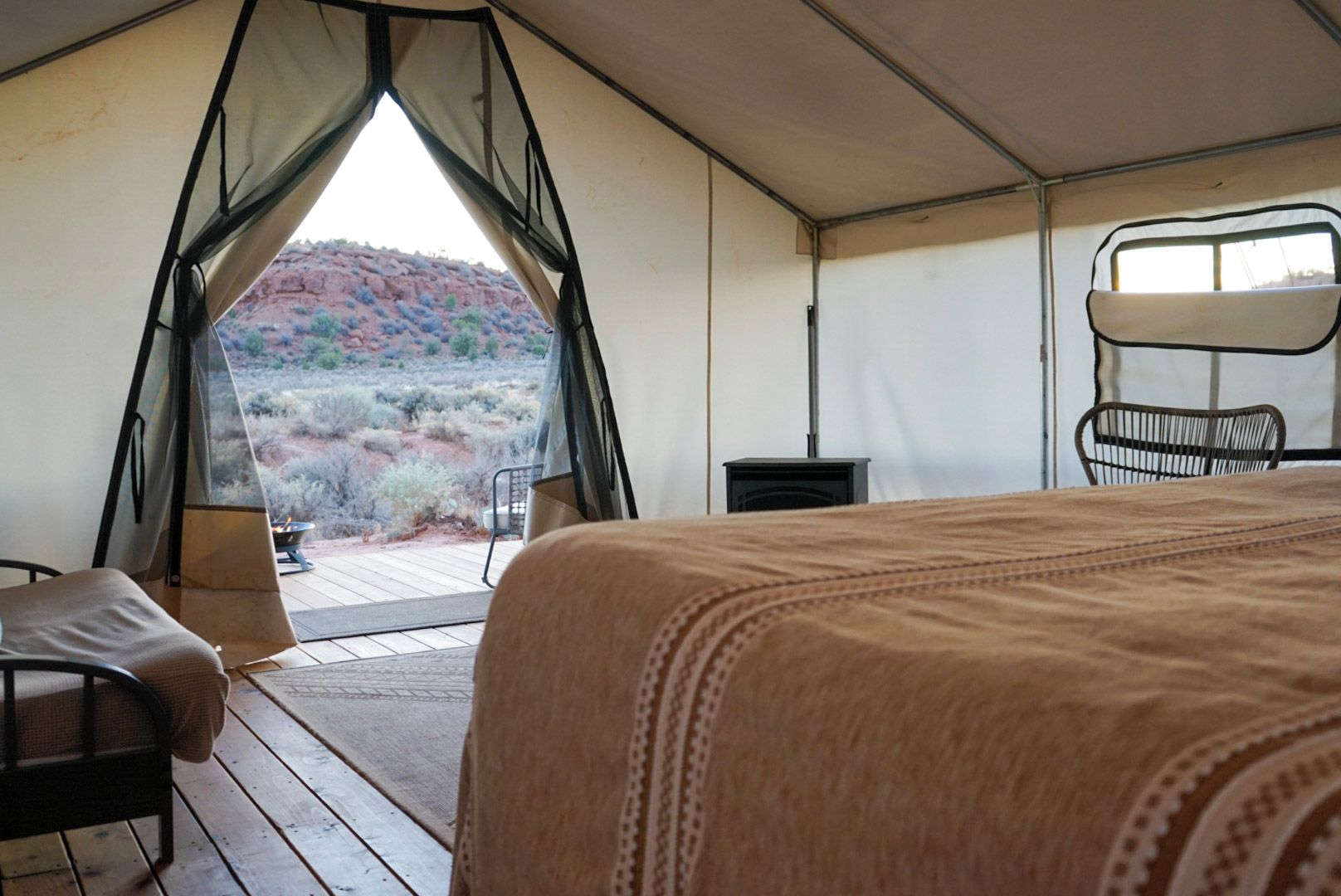 A tented room with a bed, a chair, and a view of a desert landscape.