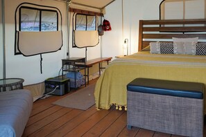 Quarto com cama, um banquinho, uma mesa e janela com cortinas.