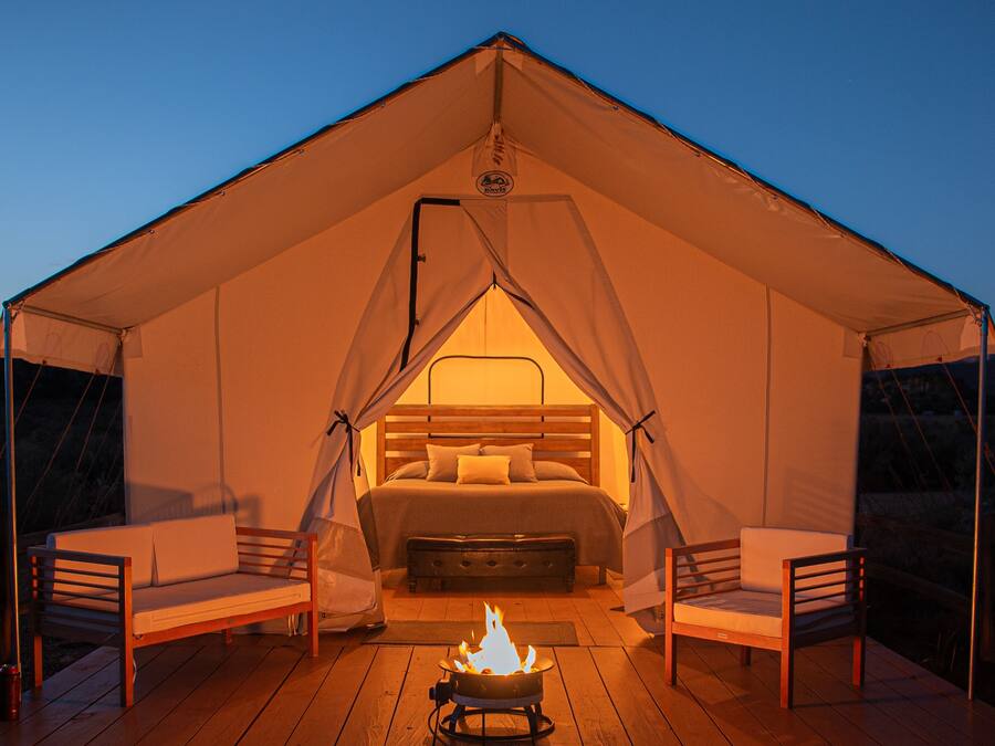 Alojamento em tenda com cama, duas cadeiras e lareira.