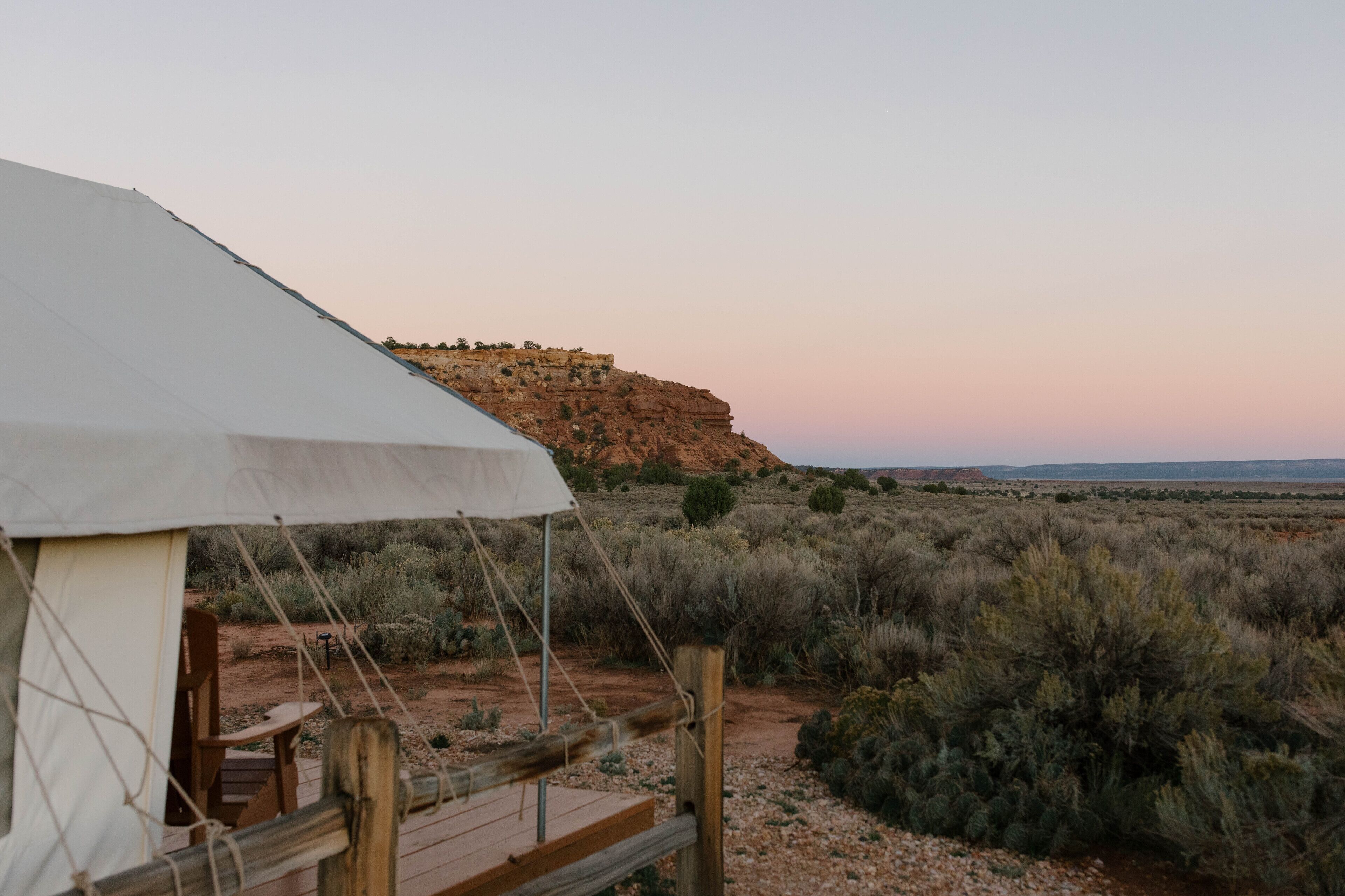 A desert camp with a wooden deck and a white tent.