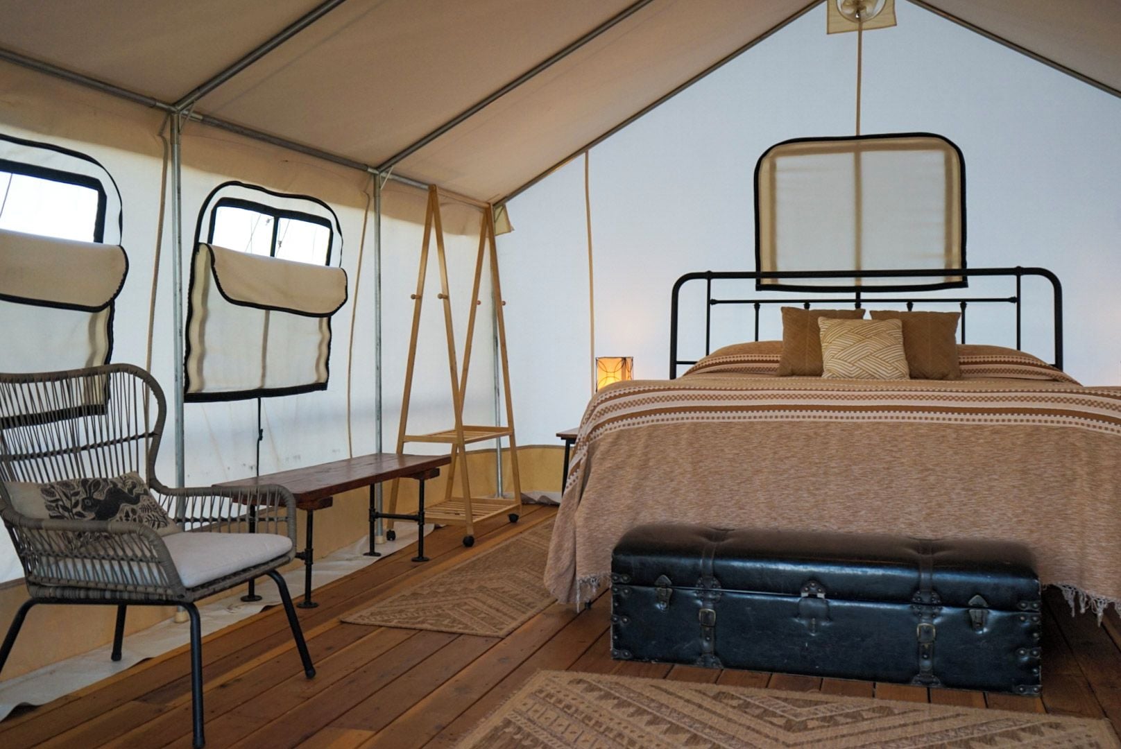 A tented room with a bed, a chair, a bench, and a table.