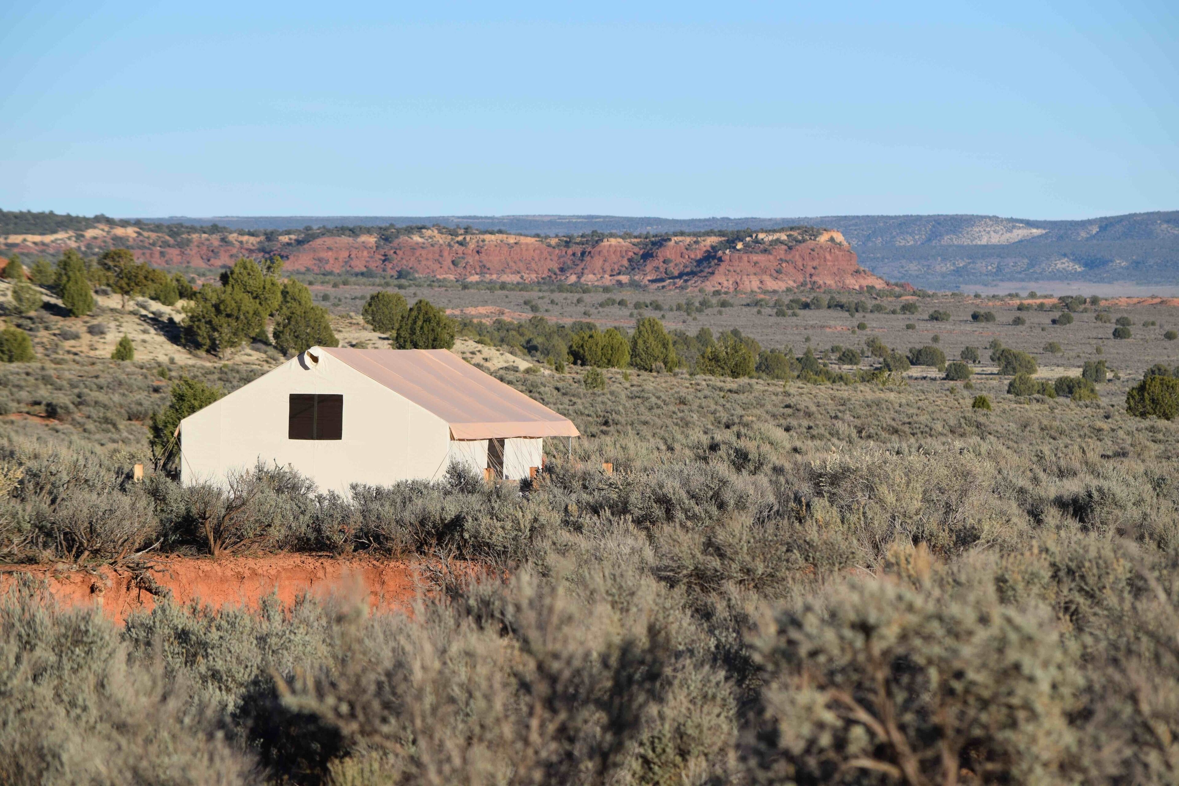 A single-story building with a flat roof, surrounded by sparse vegetation and red rock formations in the background.