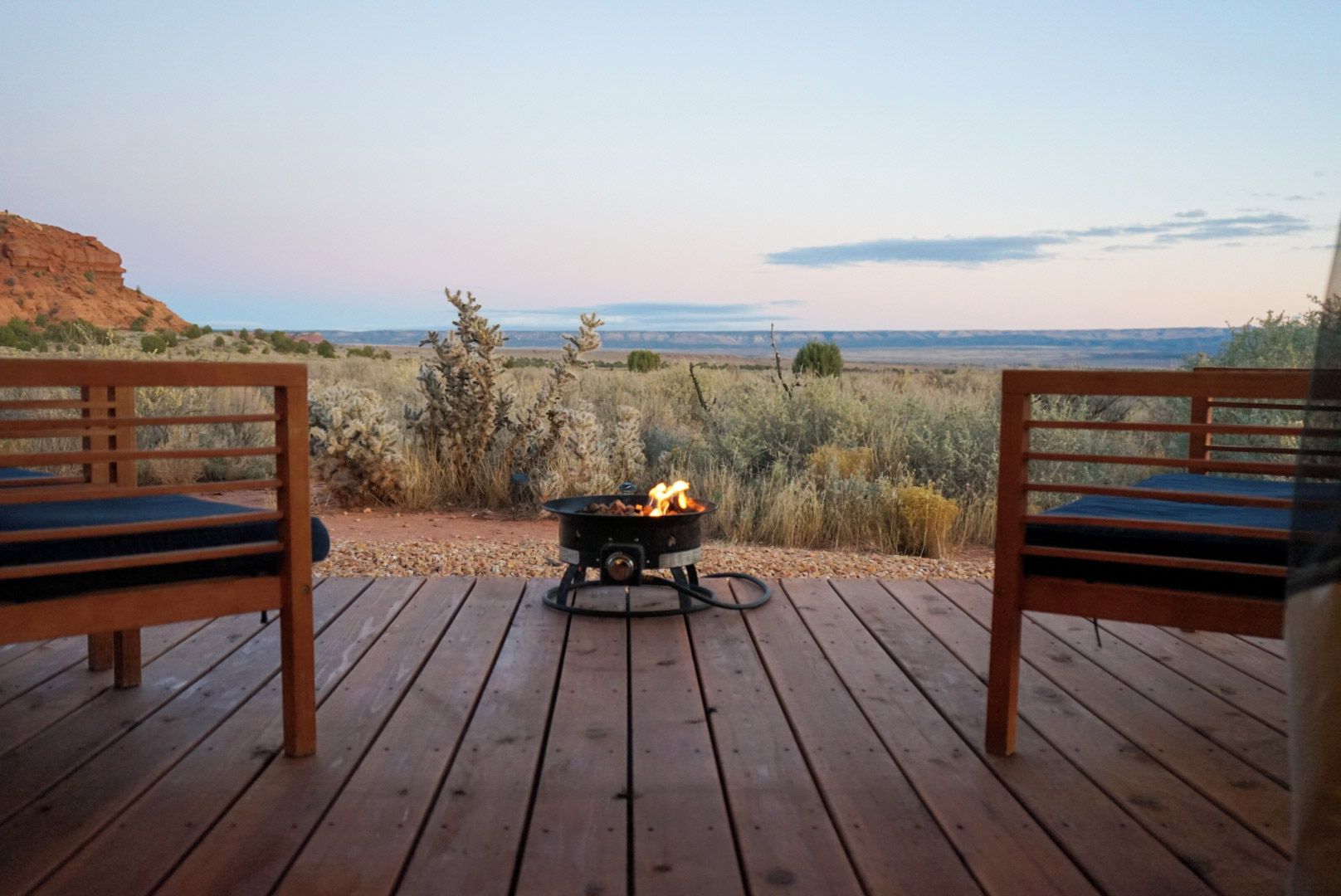 A wooden deck with two chairs facing a campfire.