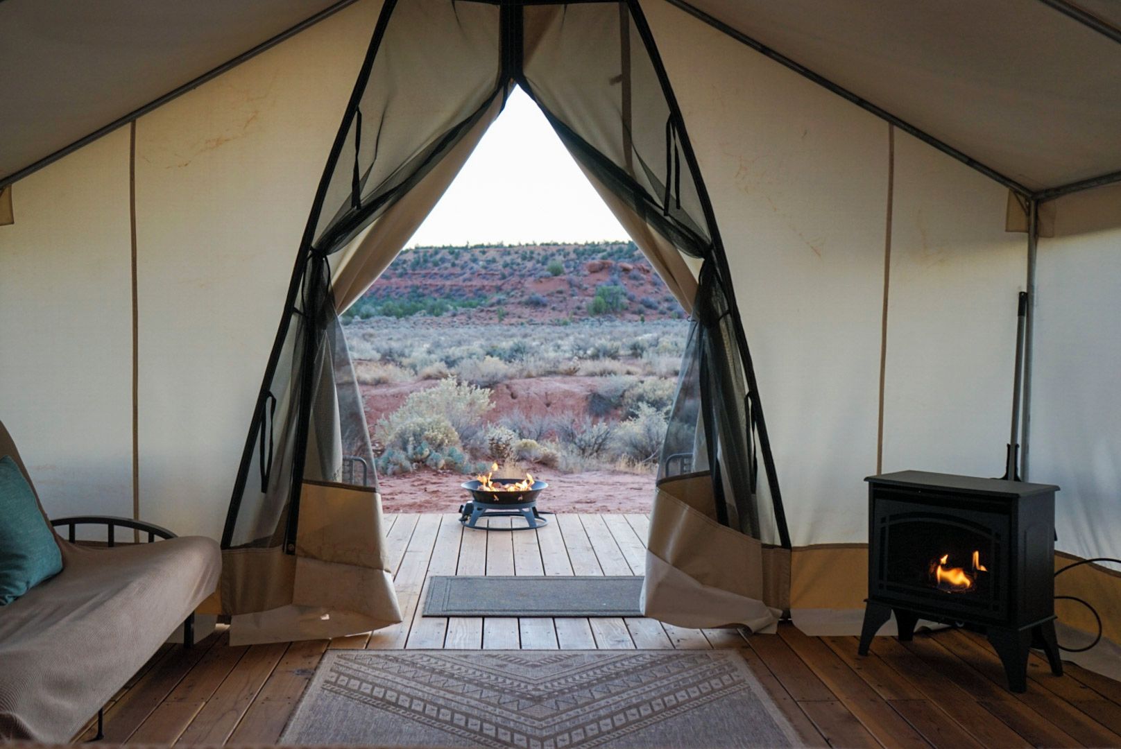 A tent with a view of a desert landscape, a fire pit, and a wood-burning stove.