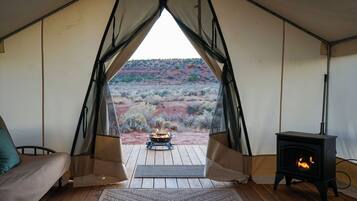 A tent with a view of a desert landscape, a fire pit, and a wood-burning stove.