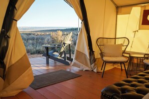 Une tente offrant une vue sur un paysage naturel, un fauteuil rembourré, une petite table et un canapé en cuir.