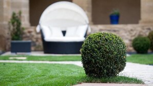 A well-maintained lawn with a neatly trimmed bush and a white outdoor chair in the background. - Chateau De La Falque (Saint-Geniez-d'Olt-et-d'Aubrac)
