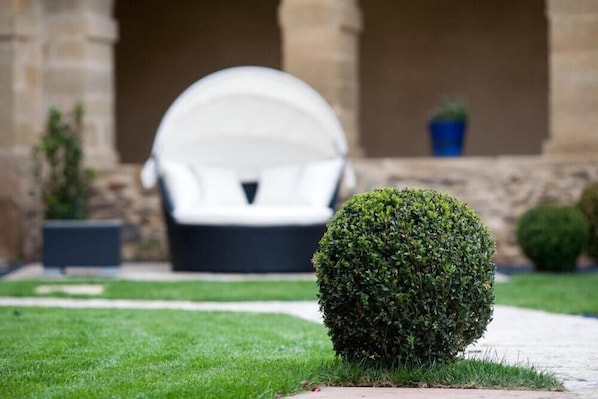 Ein gepflegter Rasen mit einem ordentlich geschnittenen Busch und einem weißen Gartenstuhl im Hintergrund.