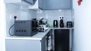 A compact kitchen with a microwave, toaster, and coffee maker on the counter, a small refrigerator, and a black cabinet above the counter. - South Harrow Apartment With Free Parking (Harrow)