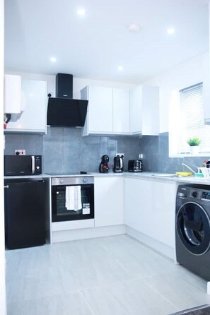 A modern kitchen with white cabinets, a built-in oven, a microwave, a coffee maker, and a washing machine.