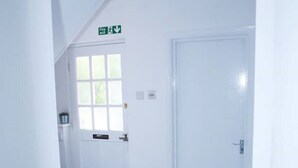 A hallway with a white door, a window, and a fire exit sign. - South Harrow Apartment With Free Parking (Harrow)