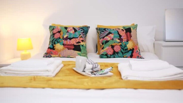 A neatly made bed with floral pillows, a tray with towels and a bottle, and a bedside lamp. - South Harrow Apartment With Free Parking (Harrow)