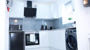 A modern kitchen with white cabinets, a microwave, an oven, a washing machine, and a coffee maker. - South Harrow Apartment With Free Parking (Harrow)