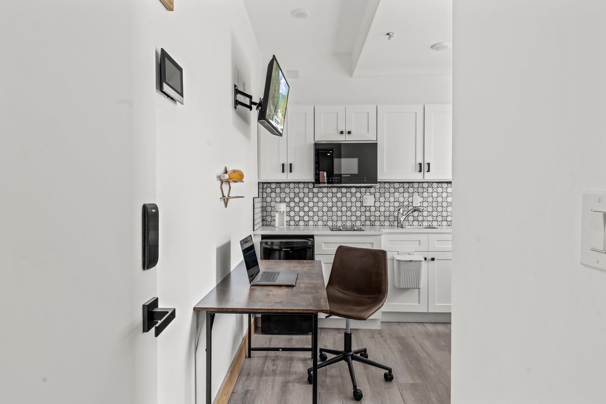 A modern kitchen with white cabinets, a black microwave, and a tiled backsplash.