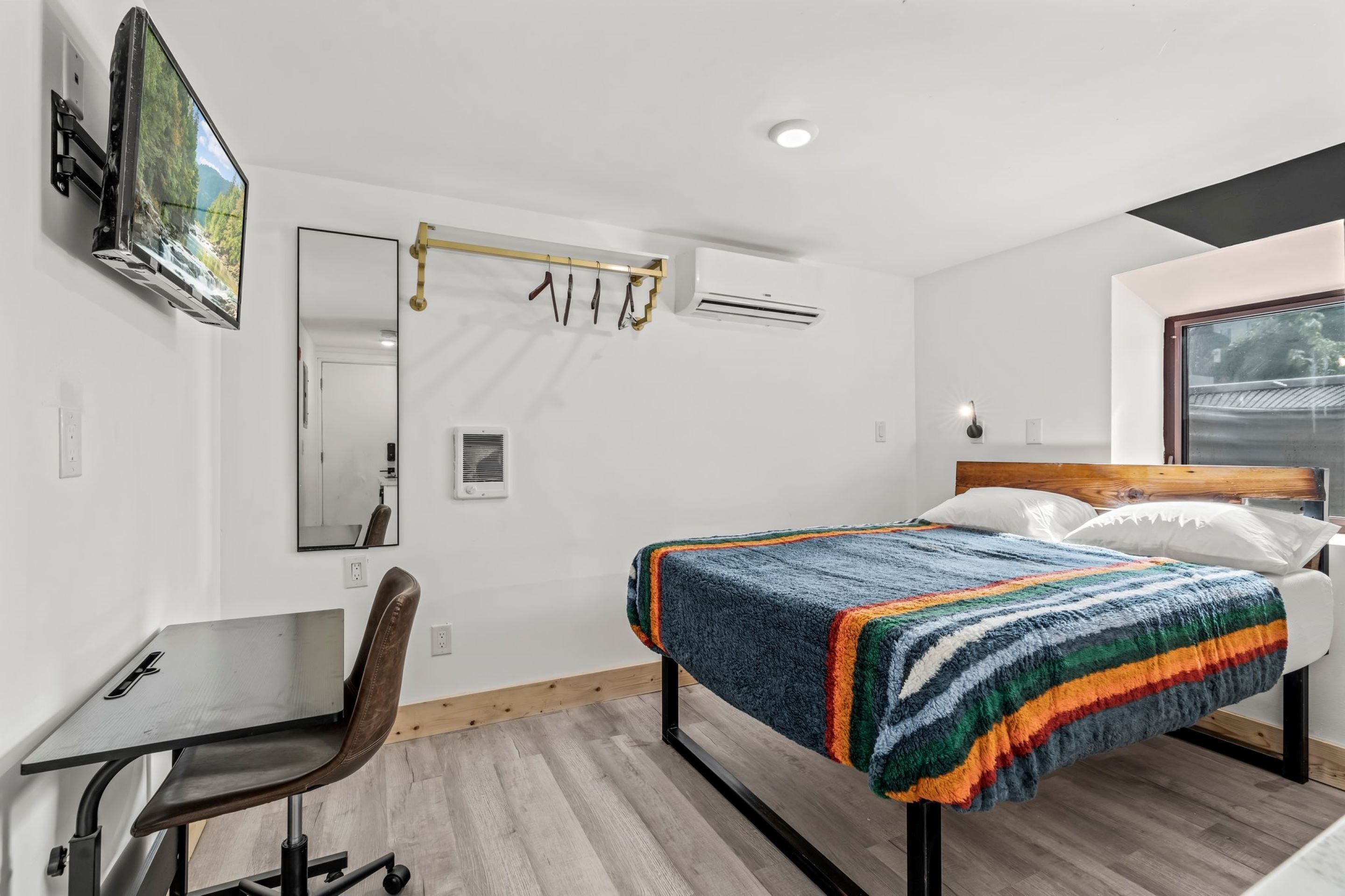 Une chambre d’hôtel moderne équipée d’un lit, d’un bureau, d’une chaise, d’une télévision et d’un miroir.