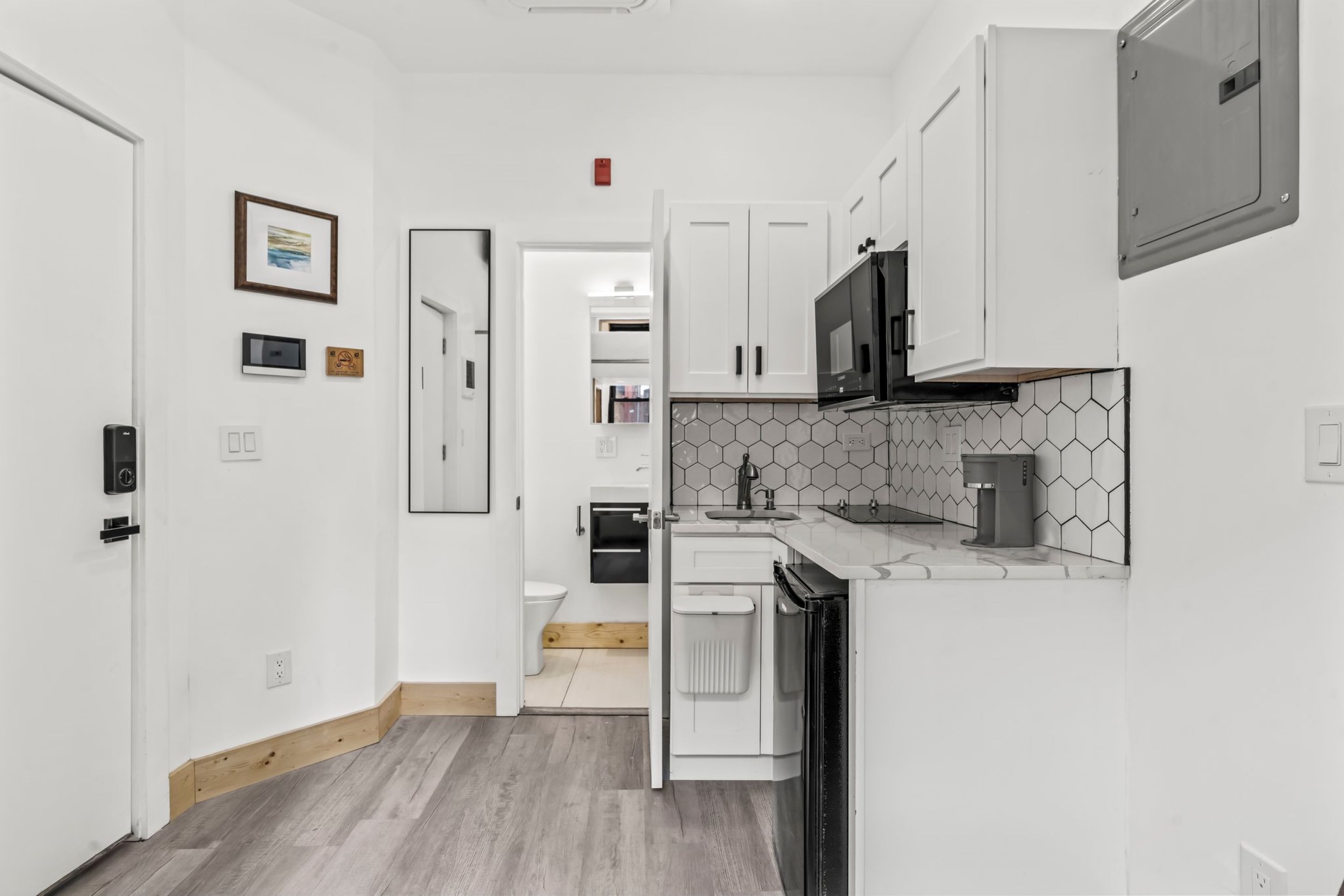 A modern kitchen with white cabinetry, a microwave, and a coffee machine.