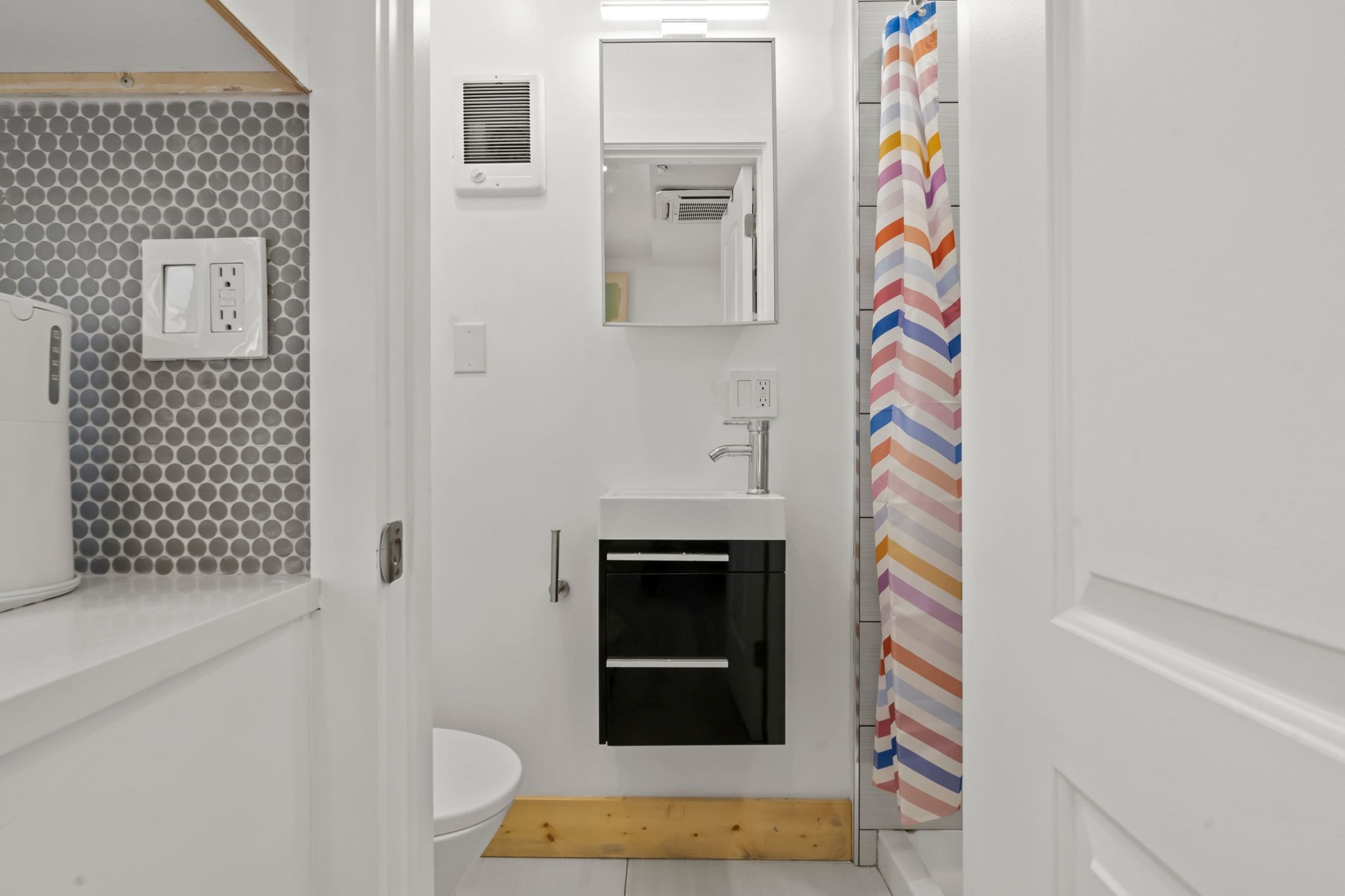 Une salle de bain moderne avec un lavabo blanc, un miroir et des toilettes. On y trouve un rideau de douche à motifs chevrons.