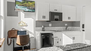 A compact kitchen with white cabinets, a microwave, and a sink. There's a television mounted on the wall displaying a nature scene.