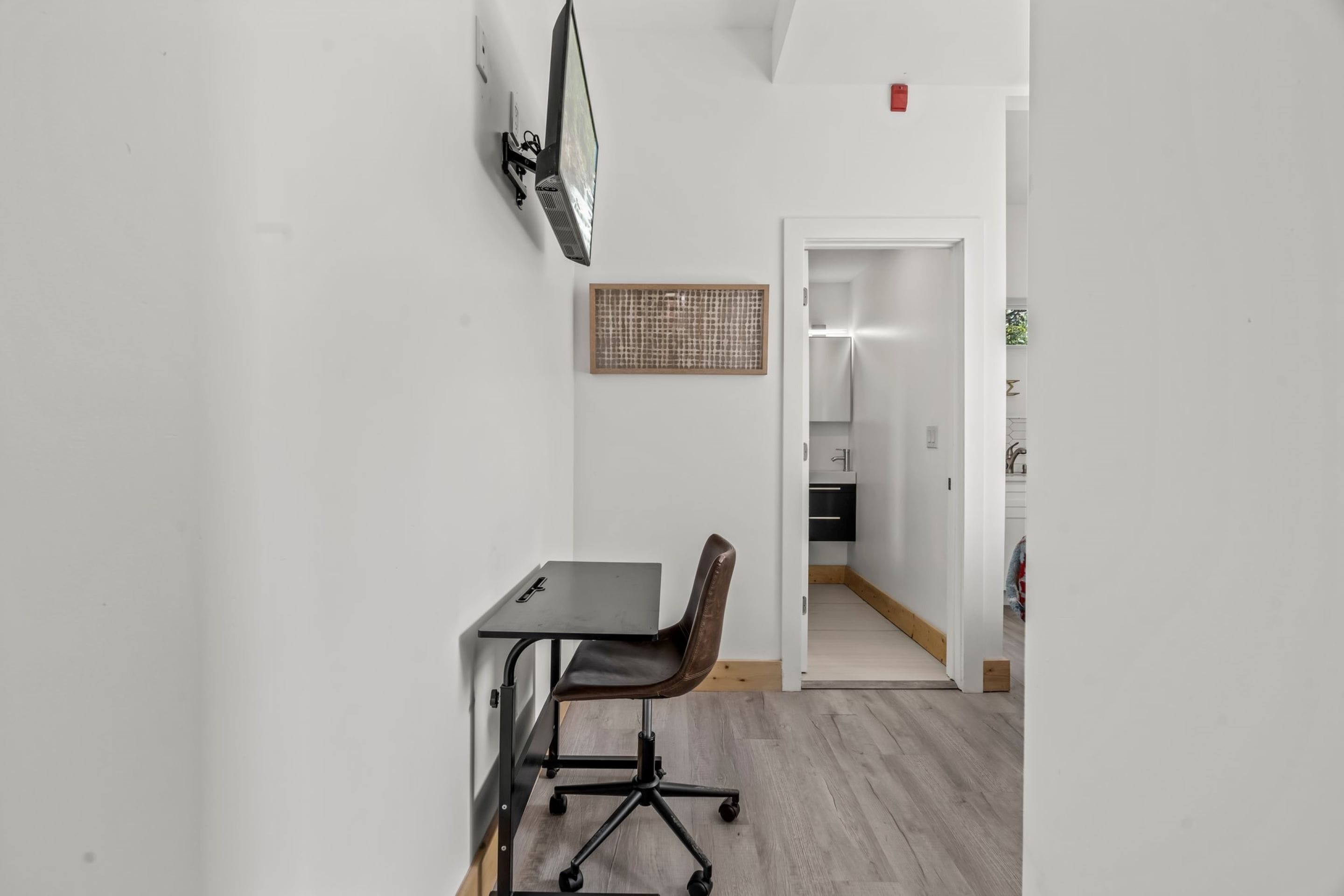 Un espacio de oficina moderno con un escritorio, una silla de oficina y un televisor montado en la pared.