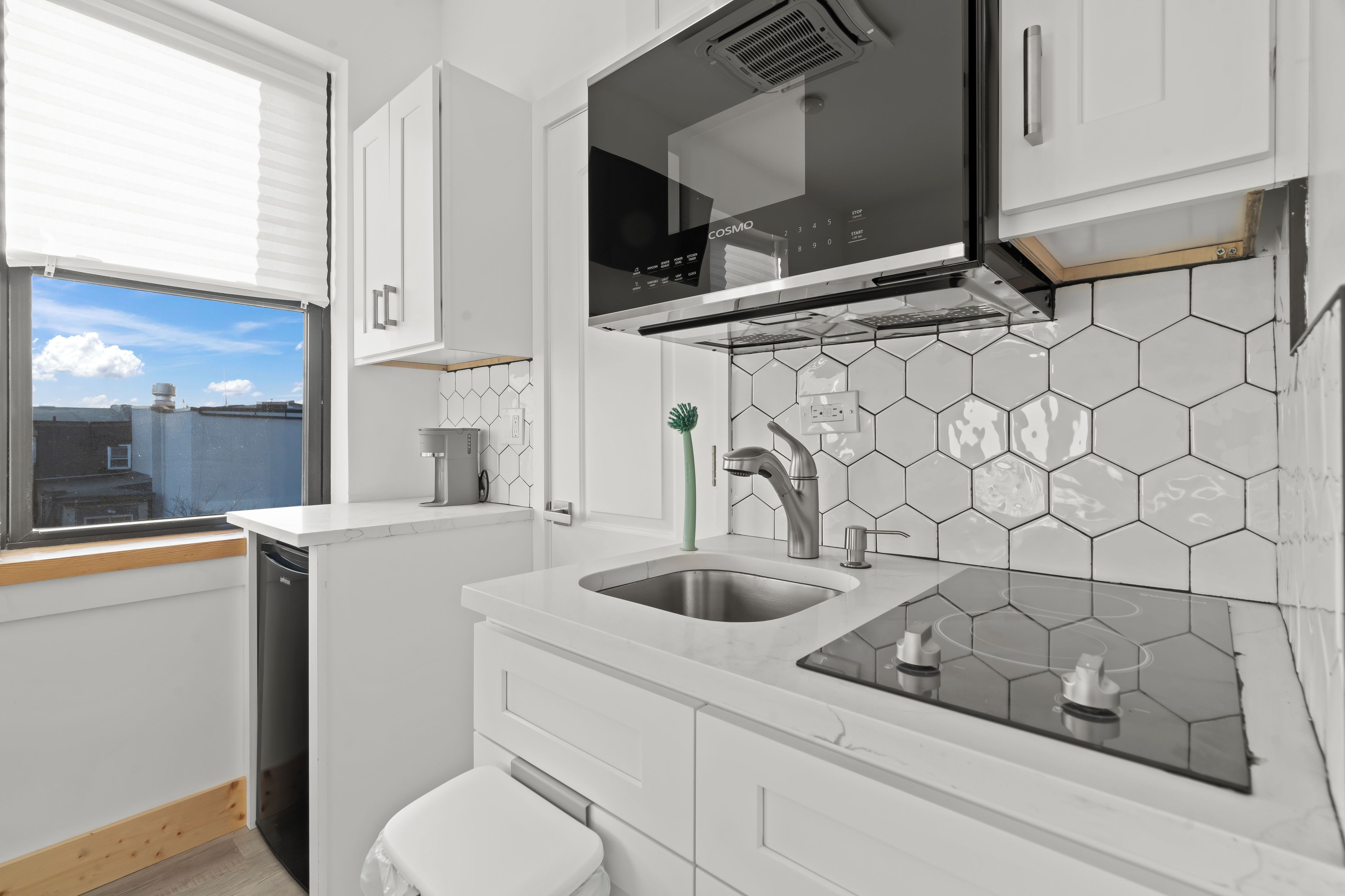 Une cuisine moderne avec des meubles blancs, une hotte noire et un dosseret de crédence en carreaux hexagonaux.