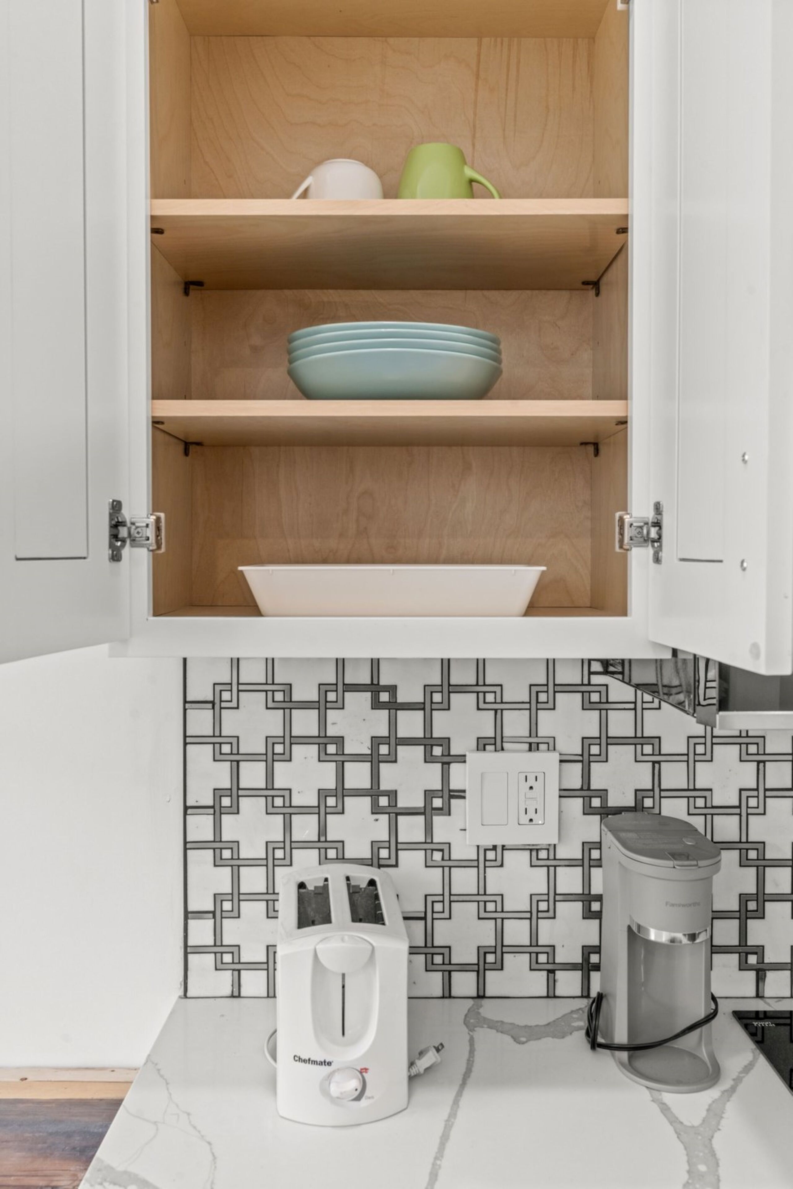 A kitchen with a white cabinet, a patterned backsplash, a coffee maker, and a toaster.