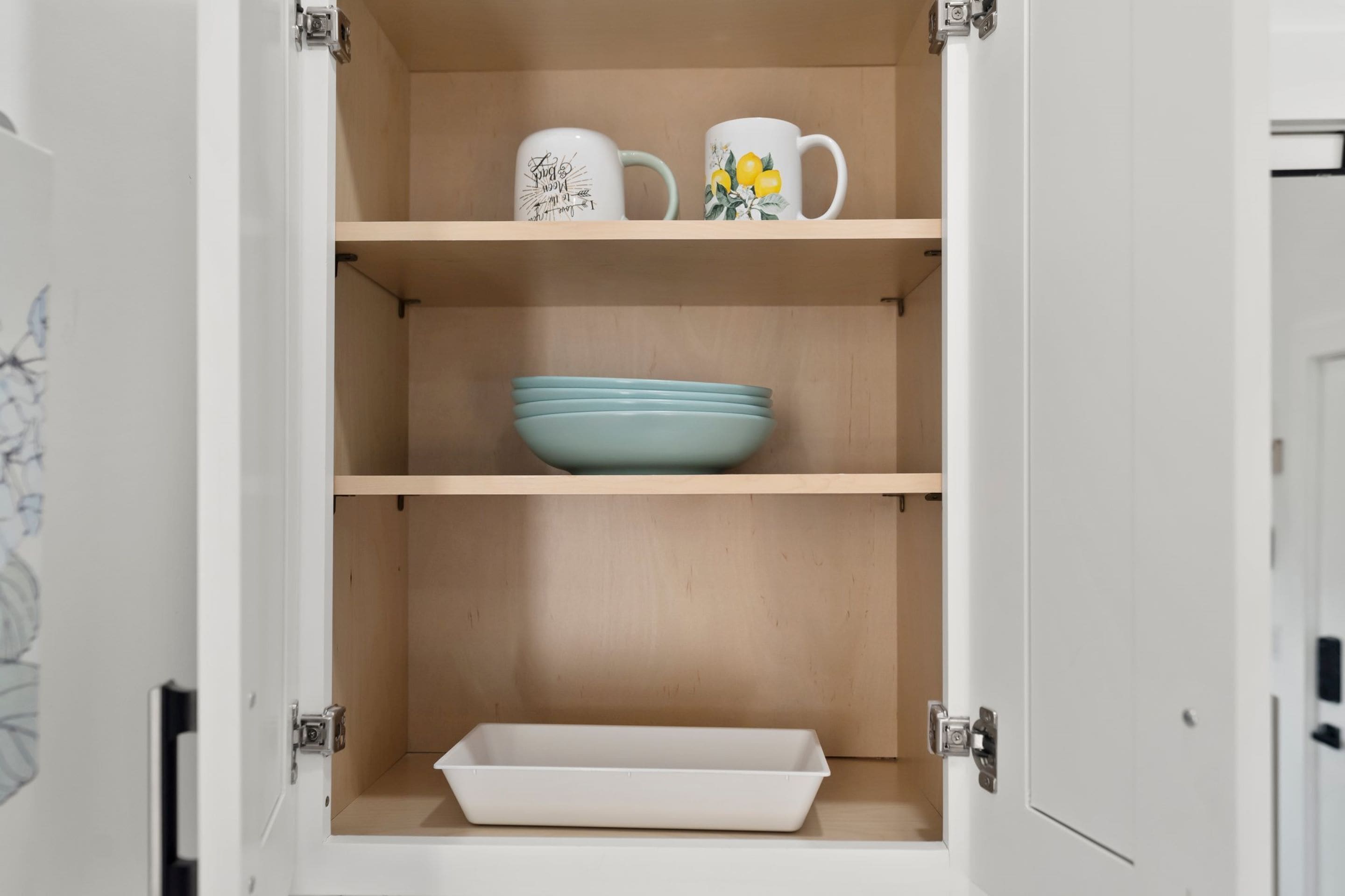 A kitchen cabinet with two mugs on the top shelf and a blue bowl on the middle shelf.