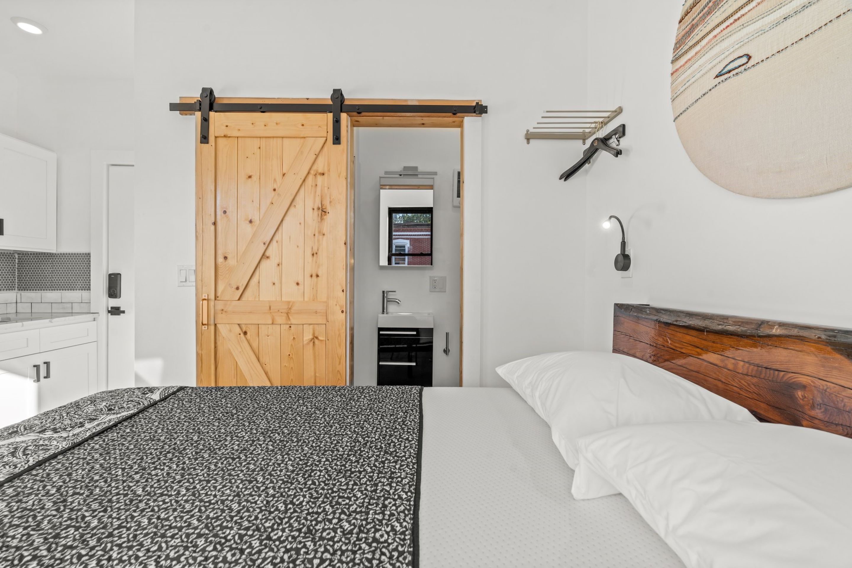 A bedroom with a wooden sliding door, a bed with white bedding, a headboard with a wooden finish, a wall-mounted TV, and a towel rack.