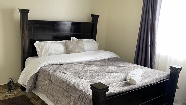 A neatly made bed with a dark headboard, a brown rug, and a patterned bedspread.