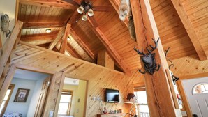 A rustic wooden interior with exposed beams, a ceiling fan, a mounted television, and a deer head decoration.