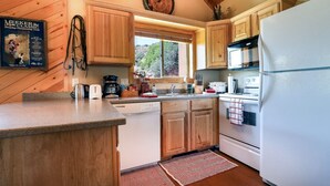 A kitchen with wooden cabinets, a white refrigerator, and a window with a view of trees.