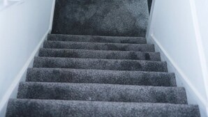 Una escalera con peldaños alfombrados y paredes blancas.