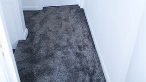 Un estrecho pasillo con una puerta blanca al final, suelo alfombrado y un ventanal con vistas a la ciudad.