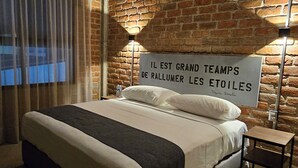 A bedroom with a large bed, a brick wall, and a sign in French. - HOTEL THE ROOF (León)