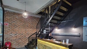 A bar area with a wooden counter, a staircase, and a brick wall. - HOTEL THE ROOF (León)