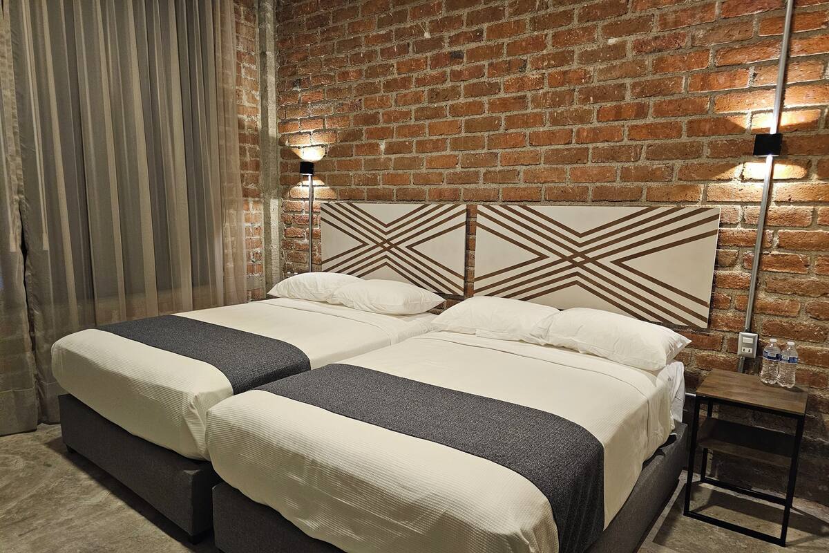 Uma cama de casal com cabeceira geométrica, uma mesa de cabeceira e uma parede de tijolos.