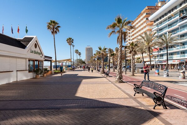 A coastal promenade with palm trees, benches, and a building with balconies. - MalagaSuite Fuengirola Beach & Sun (Fuengirola)