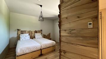 A bedroom with a wooden headboard, two beds, a hanging light fixture, and a thermostat on the wall.