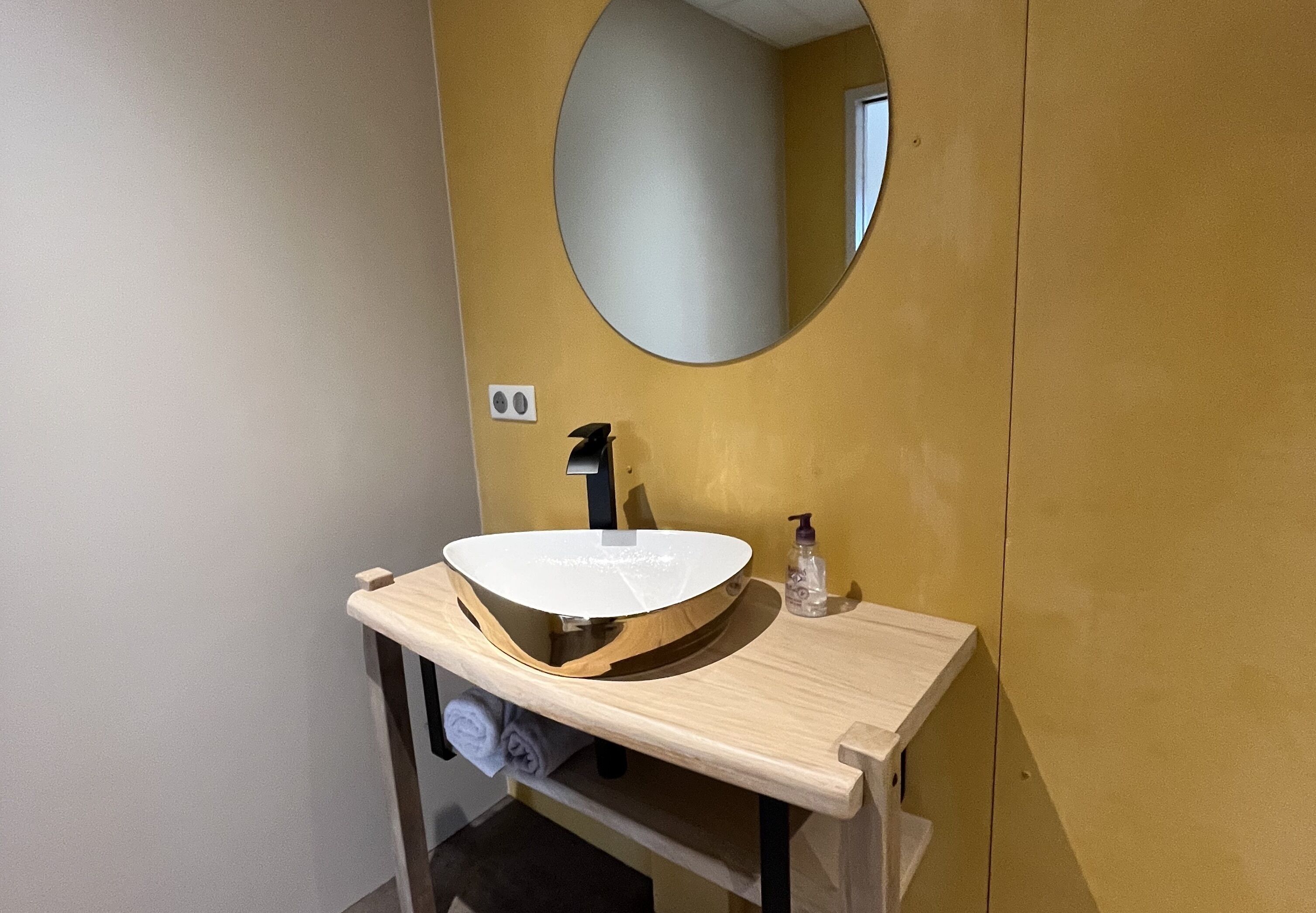 Un baño con un espejo redondo, un lavabo y un perchero para toallas.