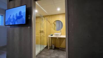 A modern bathroom with a glass shower enclosure, a round mirror, and a white sink.
