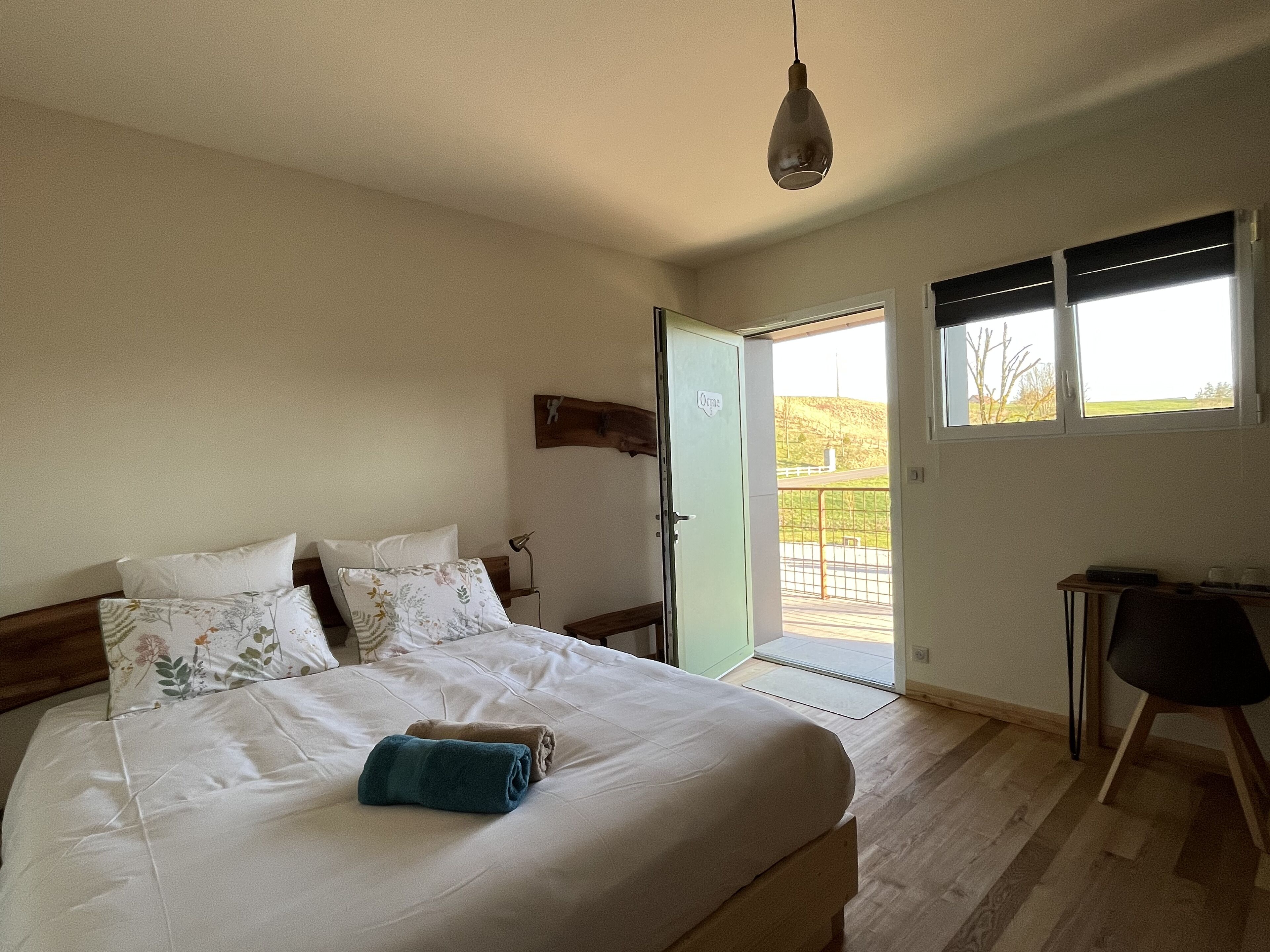 A bedroom with a bed, pillows, a bedside table, a lamp, and a view of the outdoors through a door.