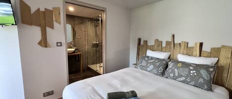 A hotel room with a bed, a wooden headboard, a bedside table with a mirror, and a shower area.