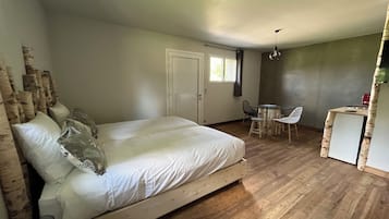 A bedroom with a wooden bed, a small dining area with a table and chairs, and a kitchenette.