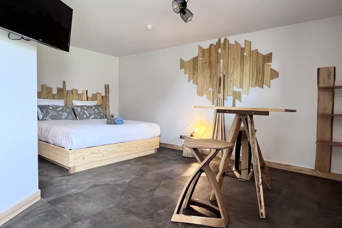 Une chambre à coucher moderne avec un lit en bois, une œuvre d’art murale originale, un petit tabouret en bois et une échelle.