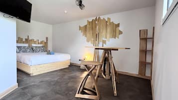 Un dormitorio moderno con una cama de madera, una pieza de arte original en la pared, un taburete de madera pequeño y una escalera.