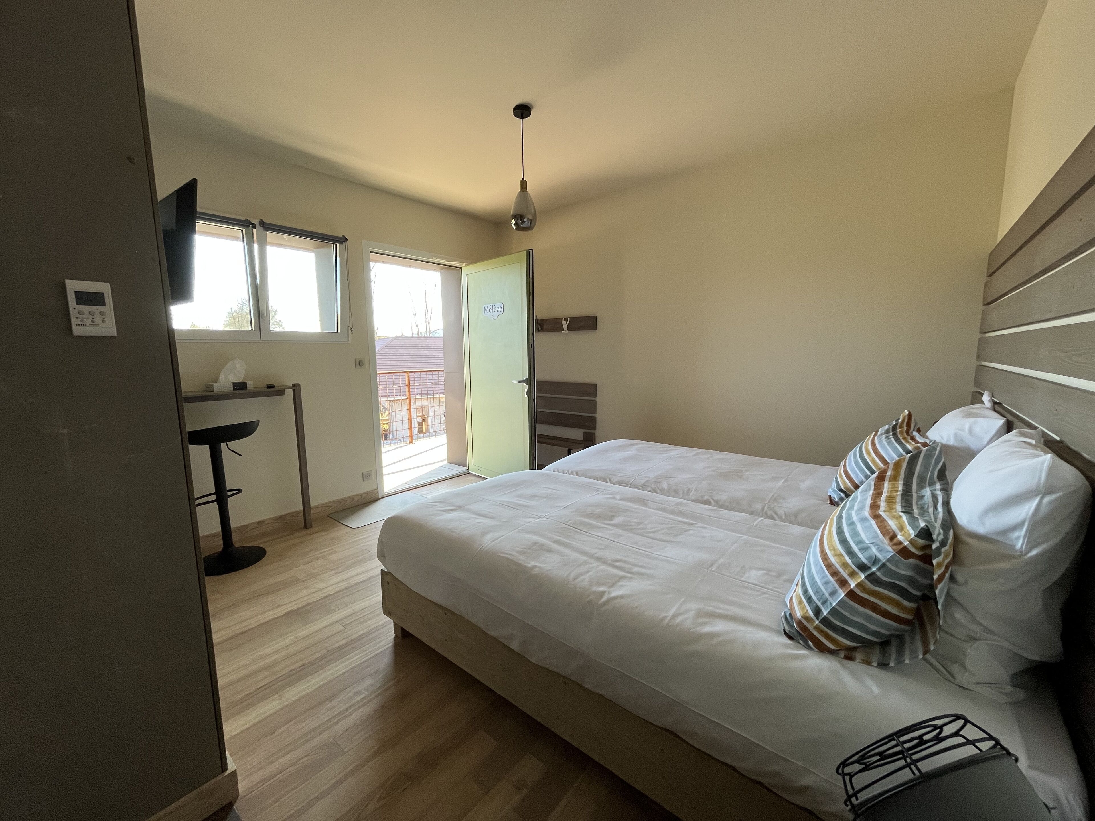 A bedroom with a bed, pillows, a window, and a door leading to an outdoor area.