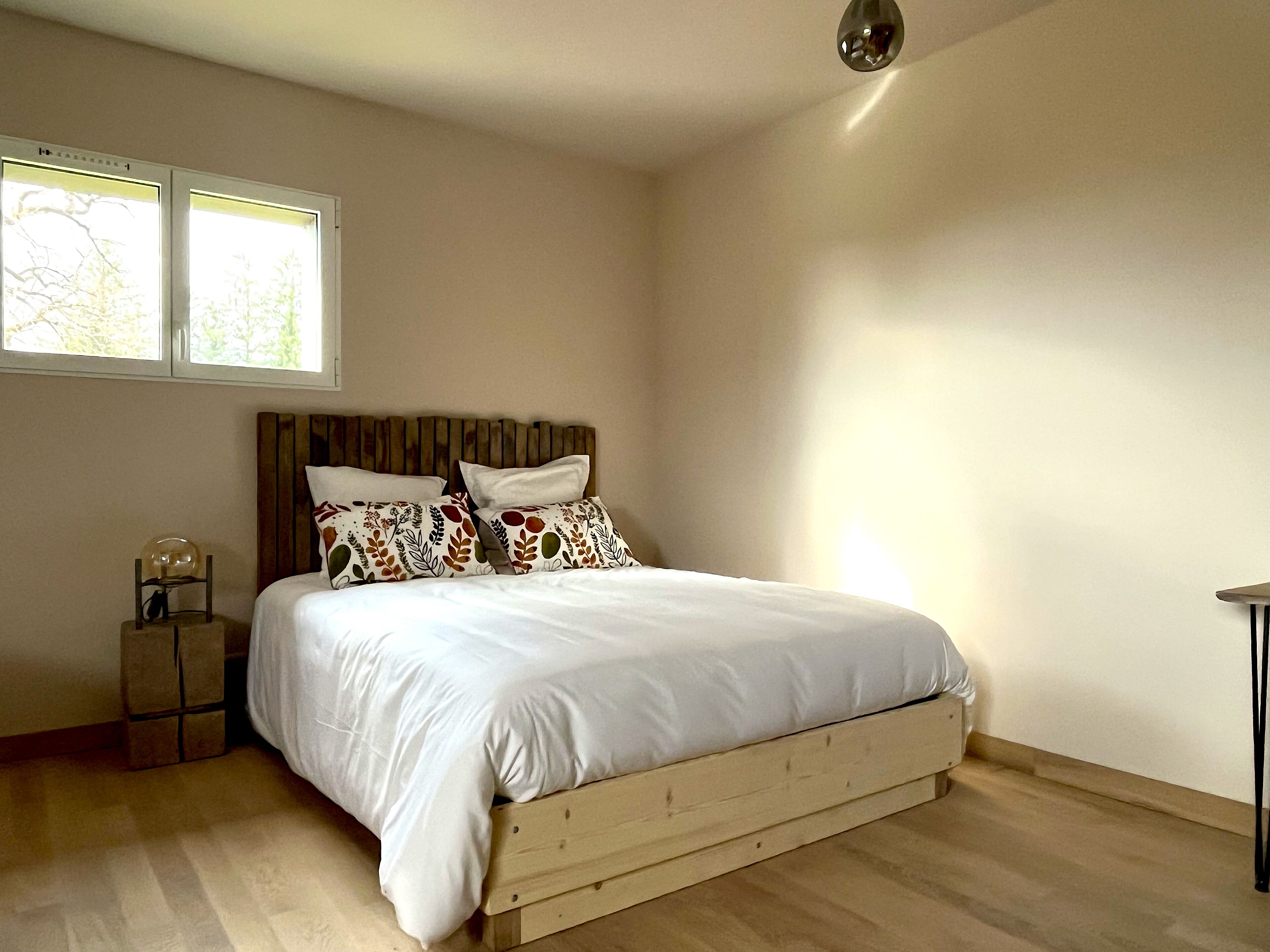 A bedroom with a wooden bed, two windows, a bedside table with a lamp, and a small table with a globe.
