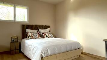 A bedroom with a wooden bed, two windows, a bedside table with a lamp, and a small table with a globe.