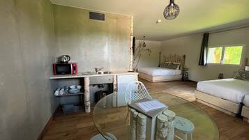 Un dormitorio moderno con una mesa de comedor de vidrio, un sofá blanco, una cama y una zona de cocina con microondas y fregadero.